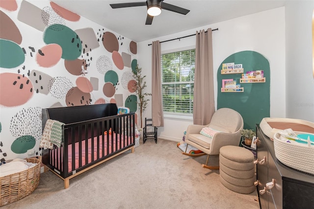 carpeted bedroom with ceiling fan and a nursery area