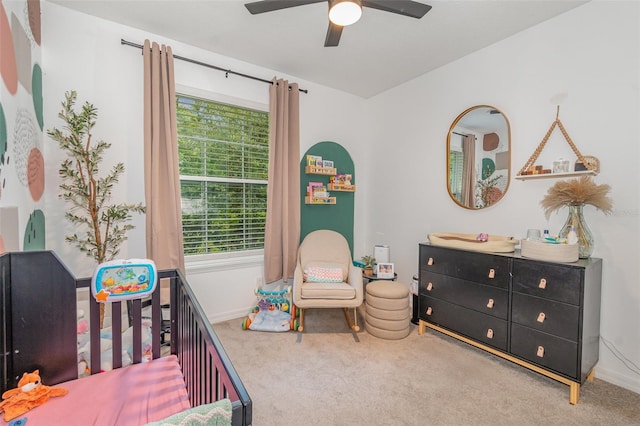 carpeted bedroom featuring a nursery area and ceiling fan