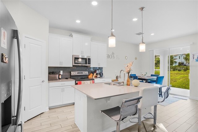 kitchen with appliances with stainless steel finishes, white cabinetry, decorative light fixtures, and an island with sink