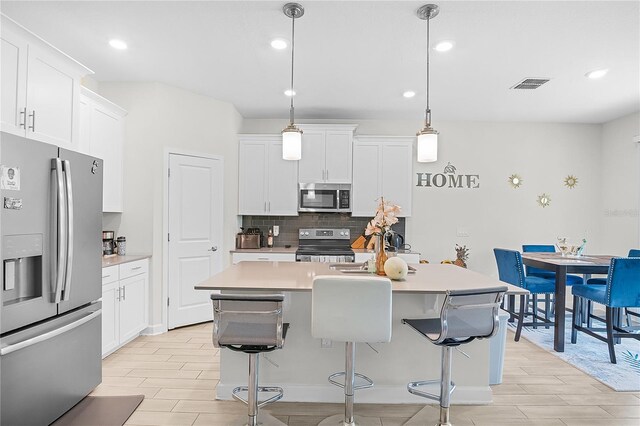 kitchen with pendant lighting, light hardwood / wood-style flooring, appliances with stainless steel finishes, a center island with sink, and white cabinets