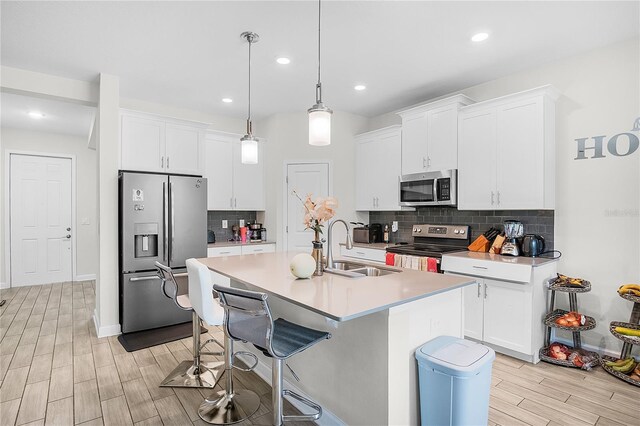 kitchen with white cabinets, light hardwood / wood-style flooring, appliances with stainless steel finishes, sink, and an island with sink