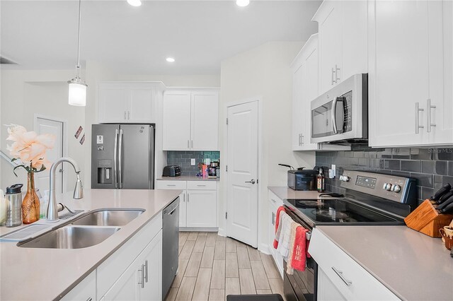 kitchen featuring white cabinets, light wood-type flooring, appliances with stainless steel finishes, sink, and pendant lighting