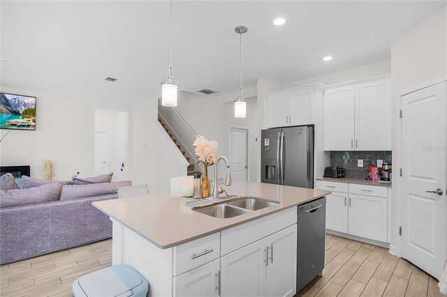 kitchen with appliances with stainless steel finishes, an island with sink, sink, white cabinetry, and light wood-type flooring