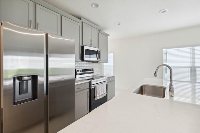 kitchen featuring decorative backsplash, gray cabinetry, light stone countertops, stainless steel appliances, and sink