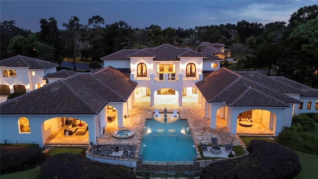 back of property at dusk featuring a tiled roof, stucco siding, a balcony, and an in ground hot tub