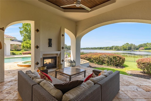 view of patio / terrace featuring ceiling fan, a water view, fence, a pool with connected hot tub, and an outdoor living space with a fireplace