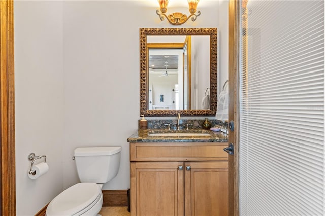 half bathroom featuring toilet, baseboards, and vanity