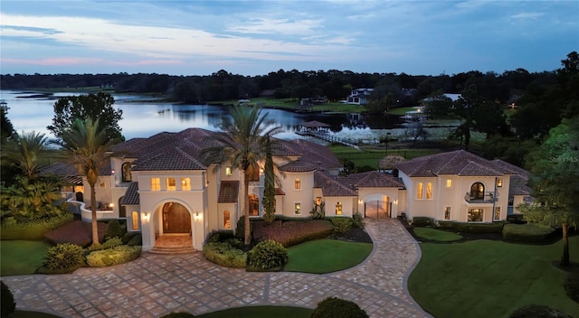 mediterranean / spanish house with decorative driveway, a water view, a lawn, and stucco siding