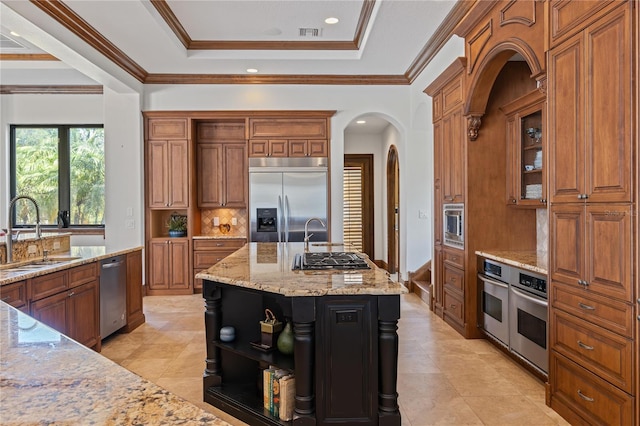 kitchen featuring an island with sink, appliances with stainless steel finishes, glass insert cabinets, light stone countertops, and a sink