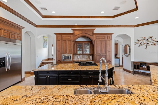 kitchen featuring built in appliances, a sink, visible vents, a tray ceiling, and glass insert cabinets