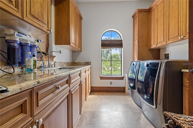 laundry area featuring light tile patterned floors, cabinet space, a sink, washer and dryer, and baseboards