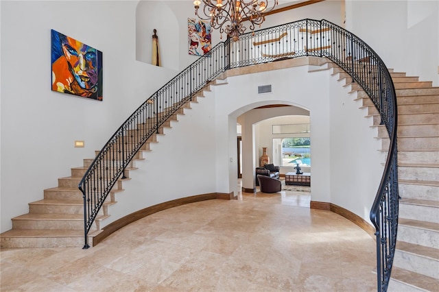 entryway with visible vents, baseboards, arched walkways, a towering ceiling, and an inviting chandelier