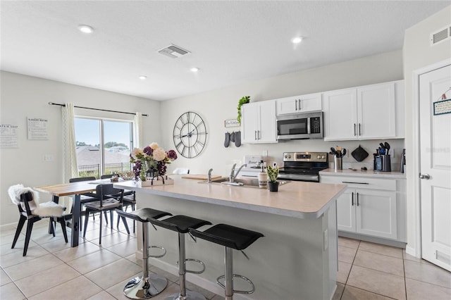 kitchen with an island with sink, white cabinets, a kitchen breakfast bar, and appliances with stainless steel finishes