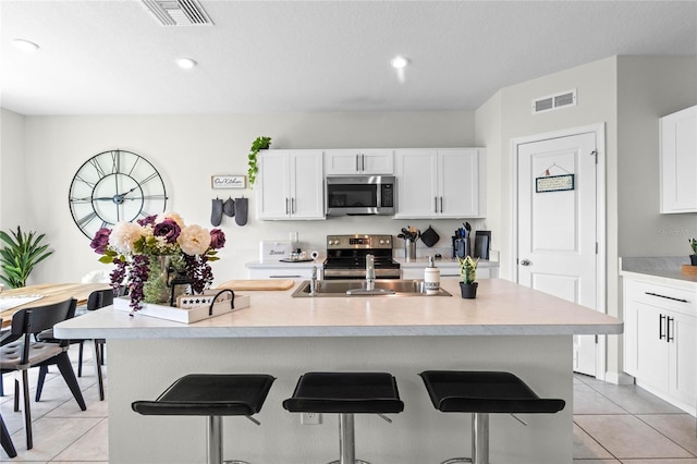 kitchen featuring white cabinets, an island with sink, light tile patterned floors, appliances with stainless steel finishes, and a kitchen breakfast bar