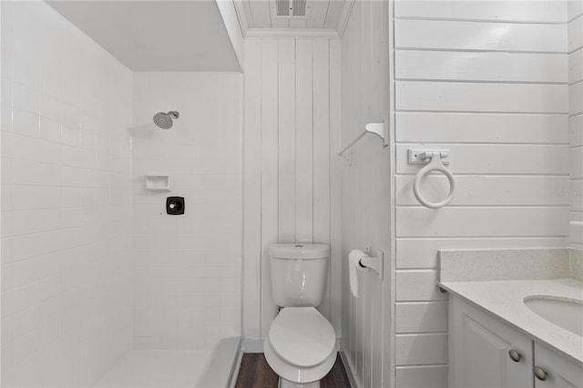 bathroom featuring vanity, a tile shower, hardwood / wood-style floors, wooden walls, and toilet