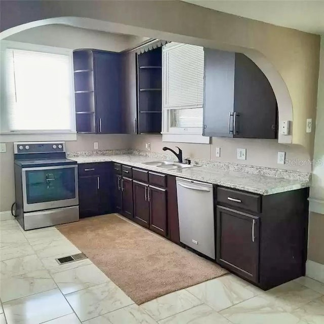 kitchen with appliances with stainless steel finishes, light stone counters, dark brown cabinetry, and sink