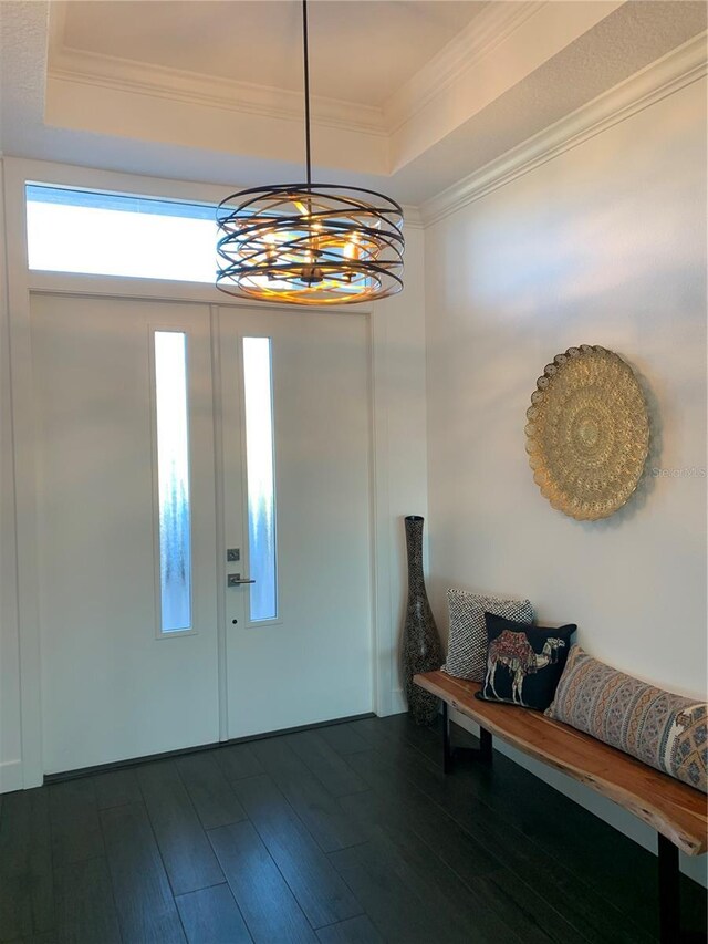 entrance foyer featuring a notable chandelier, ornamental molding, dark wood-type flooring, and a tray ceiling