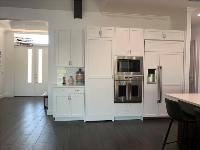 kitchen with dark hardwood / wood-style flooring, tasteful backsplash, built in appliances, white cabinets, and hanging light fixtures