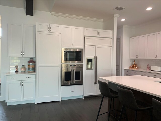 kitchen featuring tasteful backsplash, built in appliances, and white cabinetry