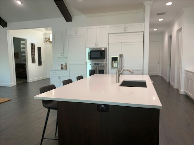 kitchen with a kitchen island with sink, sink, built in appliances, beamed ceiling, and white cabinetry