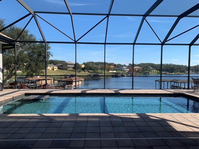 view of swimming pool featuring a patio, a water view, and glass enclosure