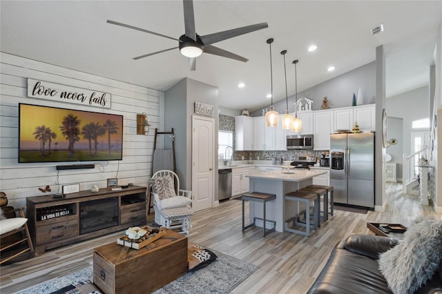 living room featuring wood walls, light hardwood / wood-style flooring, lofted ceiling, and ceiling fan