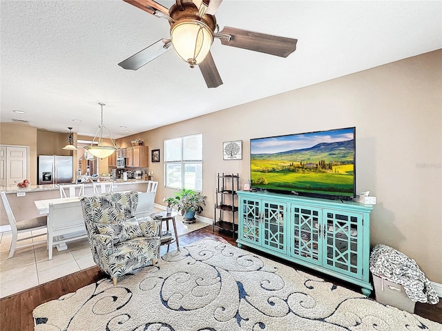 living room with ceiling fan, a textured ceiling, and light hardwood / wood-style flooring