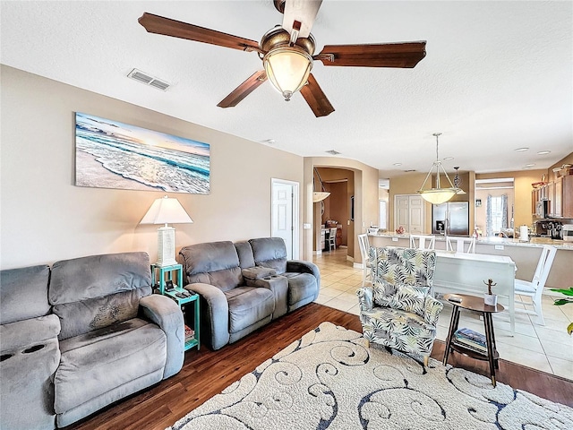 living room featuring light wood-type flooring, ceiling fan, and a textured ceiling