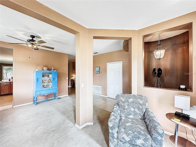 living area with a textured ceiling, ceiling fan, and light colored carpet