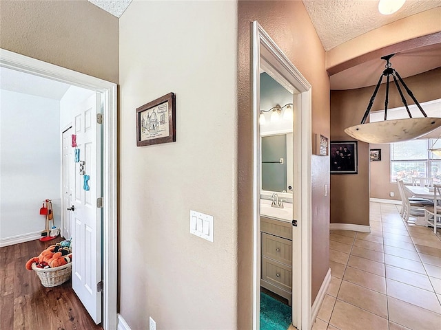 hall featuring light tile patterned flooring, sink, and a textured ceiling