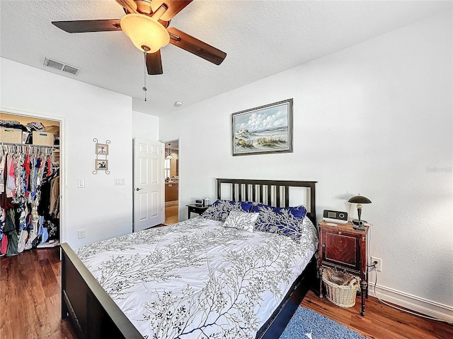 bedroom with ceiling fan, a textured ceiling, dark wood-type flooring, a walk in closet, and a closet