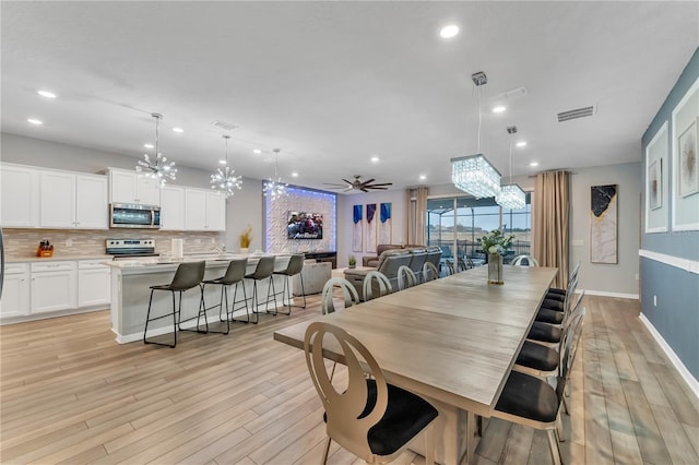 dining room featuring ceiling fan with notable chandelier and light hardwood / wood-style floors