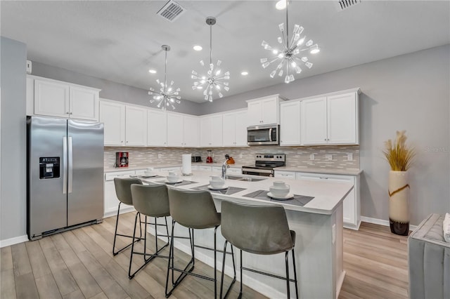 kitchen with pendant lighting, an island with sink, white cabinetry, appliances with stainless steel finishes, and light hardwood / wood-style floors