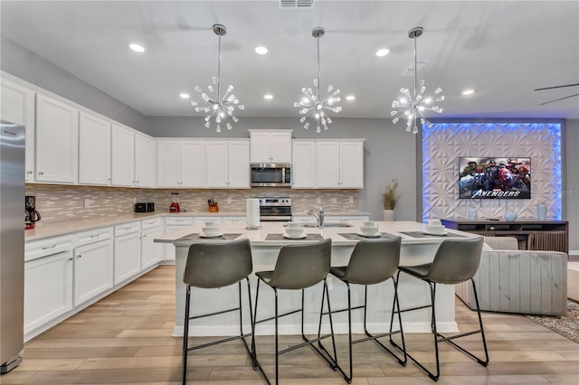 kitchen featuring pendant lighting, light wood-type flooring, a chandelier, white cabinets, and appliances with stainless steel finishes