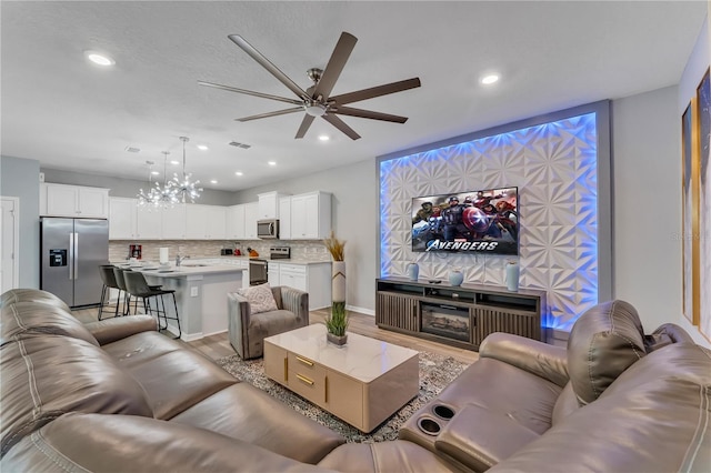 living room with ceiling fan with notable chandelier, wood-type flooring, and sink