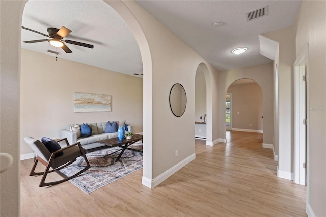 living room featuring ceiling fan, a textured ceiling, and light hardwood / wood-style floors