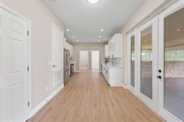 hall featuring a textured ceiling, light wood-type flooring, and french doors