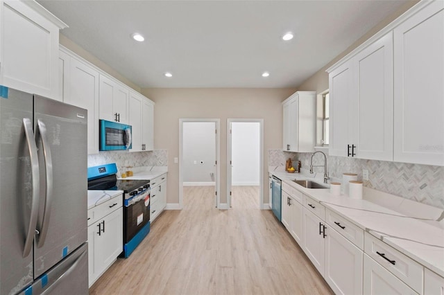 kitchen with white cabinets, stainless steel appliances, sink, and light hardwood / wood-style flooring