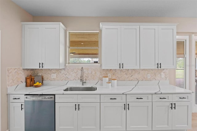 kitchen with white cabinetry, backsplash, light stone countertops, stainless steel dishwasher, and sink