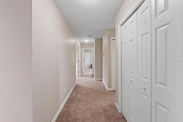 hallway featuring light colored carpet and a textured ceiling