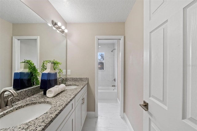 bathroom with a textured ceiling, vanity, and tiled shower / bath