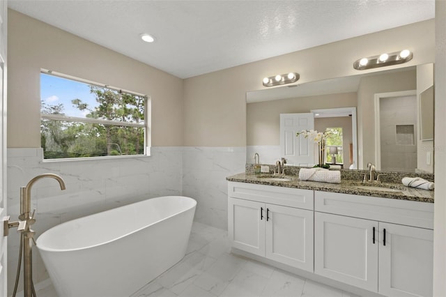 bathroom featuring tile walls, a textured ceiling, a bath, and vanity