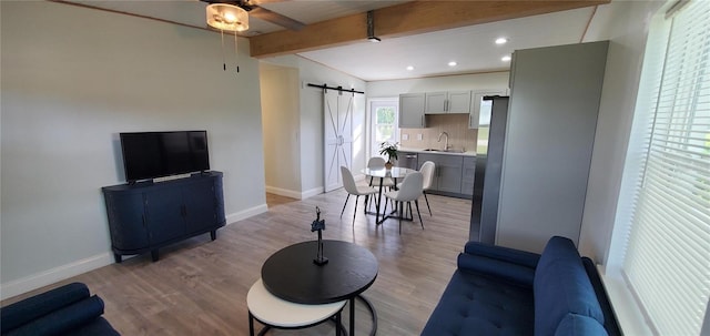 living room featuring a barn door, sink, beamed ceiling, and light wood-type flooring