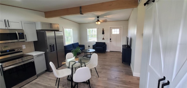 kitchen with lofted ceiling with beams, light hardwood / wood-style flooring, gray cabinets, a barn door, and stainless steel appliances