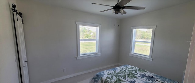 unfurnished bedroom featuring a barn door, baseboards, and a ceiling fan