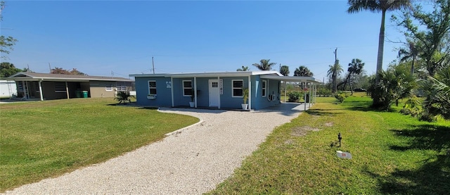 view of front facade with a carport, gravel driveway, and a front lawn