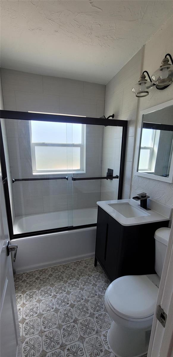 bathroom featuring shower / bath combination with glass door, toilet, vanity, a textured ceiling, and tile patterned flooring