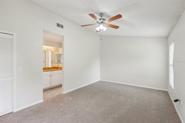 unfurnished bedroom with vaulted ceiling, a closet, ceiling fan, ensuite bath, and light carpet