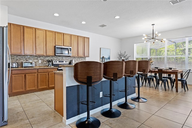 kitchen with an inviting chandelier, decorative light fixtures, light stone countertops, stainless steel appliances, and a kitchen breakfast bar