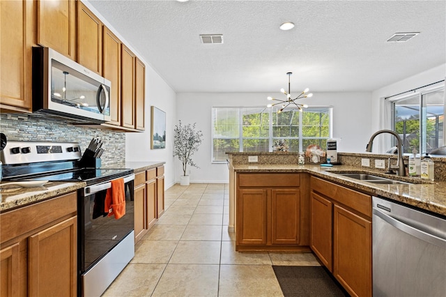 kitchen featuring light stone counters, stainless steel appliances, a notable chandelier, sink, and tasteful backsplash